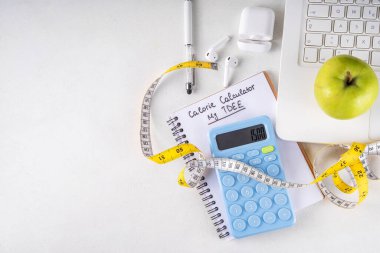 Kalori hesap makinesi, sağlıklı TDEE konsepti. Toplam günlük enerji harcamalarına dayanan kalori hesaplaması, hesap makinesi, defter, mezura, elma. Sağlıklı kilo verme diyeti arka planı
