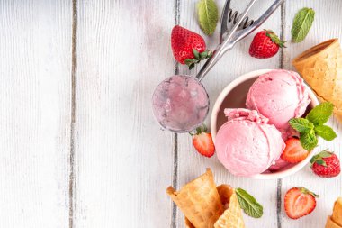 Yaz ferahlatıcı soğuk tatlı, lezzetli ve aromatik çilekli dondurma, seramik kasede ev yapımı meyve şerbeti, taze çilekler, beyaz ahşap arka planda dondurma külahları.
