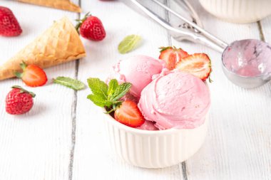 Yaz ferahlatıcı soğuk tatlı, lezzetli ve aromatik çilekli dondurma, seramik kasede ev yapımı meyve şerbeti, taze çilekler, beyaz ahşap arka planda dondurma külahları.