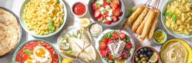 Farklı Akdeniz yemekleri: zeytin, mozarella domates salatası, Yunan salatası, makarna, tortellini ravioli, pizza, pita sandviçi, şiş kebap, shakshuka, humus, üst manzara