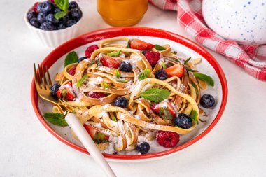 Viral modaya uygun spagetti krepleri taze böğürtlenli, yaz tatlı kahvaltı ya da öğle yemeği tarifi fikri, ev yapımı krep beyaz mutfak masasında pudra şekerli ve ballı spagetti şeklinde.