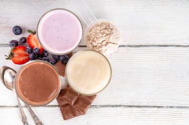 Hızlı ve basit protein pudingi. Sağlıklı yaz soğuk tatlısı. Üç bardak vanilyalı, çikolatalı ve çilekli puding, çikolata dilimleri, taze çilek, yabanmersini, protein tozu