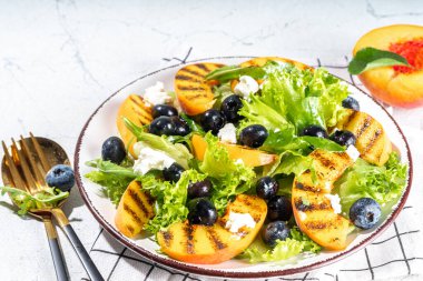 Summer peach salad. Fresh raw green salad with lettuce, arugula, grilled peach wedges, blueberry, feta cheese and honey