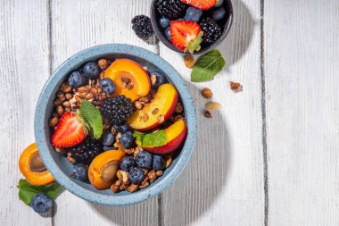 Meyve ve böğürtlenli granola kahvaltısı, yaz tatili lezzetli kahvaltı kasesi bol meyve ve böğürtlenli, süt testisi beyaz ahşap masada.
