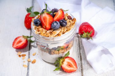 Yaz meyveleri kahvaltılık gevrek yoğurt katmanlı tatlı, yulaf taneli granola, çilek, ahşap masa arkasındaki yabanmersini fotokopi alanı.