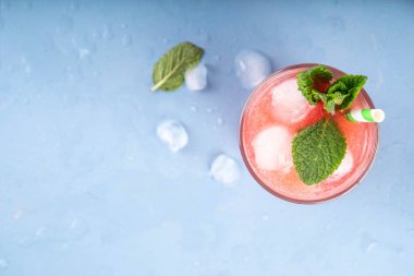 Ev yapımı karpuz limonatası, ferahlatıcı tatlı yaz içeceği, naneli buzlu karpuz suyu ve çizgili kamış, açık mavi ve ahşap arka plan, kopyalama alanı. 