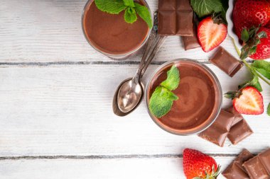 Ev yapımı çikolatalı puding, seramik porsiyonlu kase içinde mutfak masasında, taze çilek, nane ve çikolata dilimleri ile.