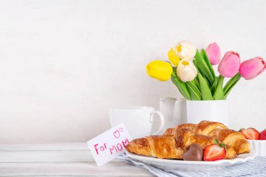 Anneler Günü kahvaltı arka planında kruvasan, çilek, çikolata, kahve fincanı, bir buket lale çiçeği, sürpriz ve hediye olarak annem için 