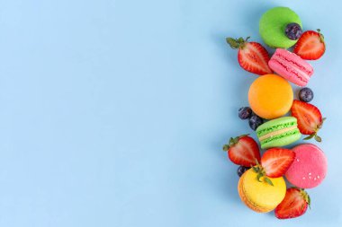 Taze meyveli, parlak ve renkli badem kurabiyesi tatlısı. Açık mavi arka planda pembe, turuncu, sarı ve şam fıstıklı yeşil, lezzetli makaron kurabiyeleri kopyalama alanı