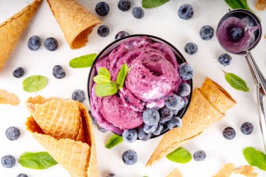 Yaban mersini zengini kremalı şerbet, taze böğürtlenli lezzetli yaban mersini dondurması, nane yaprağı ve beyaz masa fotokopi alanı üzerinde dondurmalı waffle konileri.