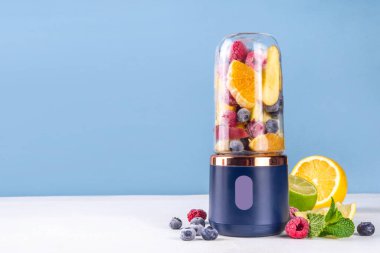 Portatif blender, meyve suyu, meyve suyu ve milkshake 'te sağlıklı meyve suyu ve meyve suyu. Şeffaf blender bardakta meyveler ve masa arkasında taze meyve suyu bardakları.
