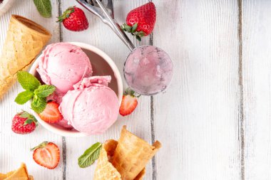 Yaz ferahlatıcı soğuk tatlı, lezzetli ve aromatik çilekli dondurma, seramik kasede ev yapımı meyve şerbeti, taze çilekler, beyaz ahşap arka planda dondurma külahları.