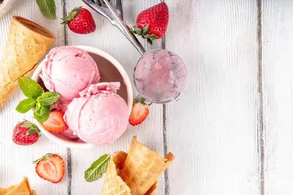 Yaz ferahlatıcı soğuk tatlı, lezzetli ve aromatik çilekli dondurma, seramik kasede ev yapımı meyve şerbeti, taze çilekler, beyaz ahşap arka planda dondurma külahları.