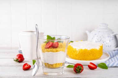 Klasik cam kaplı cheesecake, taze çilekli ve altın kurabiyeli. Katmanlı cheesecake tatlısıyla beyaz ahşap masa üzerinde taze çilekler fotokopi alanı