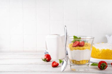 Klasik cam kaplı cheesecake, taze çilekli ve altın kurabiyeli. Katmanlı cheesecake tatlısıyla beyaz ahşap masa üzerinde taze çilekler fotokopi alanı