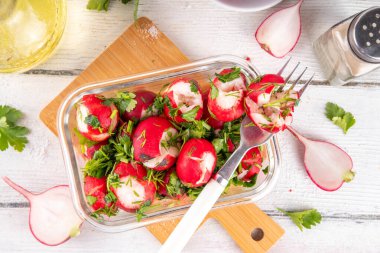 Viral ezilmiş turp salatası. Soya soslu marine edilmiş bahar turpu, maydanoz, sarımsak, zeytinyağı ve dereotu. Modaya uygun sağlıklı vegan yemeği, yaratıcı moda sebze salatası fikri, beyaz ahşap masada.