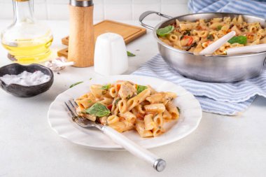 Son moda viral benimle tavuk makarnası evlen. Bir tencere yumuşak makarna ve kremalı ve peynirli sulu tavuk parçaları, sarımsaklı güneşte kurutulmuş domates sosu, nükteli fesleğen yaprağı, tabak ve demlikte.