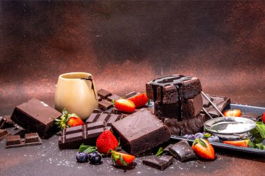 Böğürtlenli siyah çikolatalı kek. Üzerine çikolata sosu serpiştirilmiş ev yapımı kek kurabiyeleri ve koyu arkaplanda taze çilek, yabanmersini, fotokopi alanı.