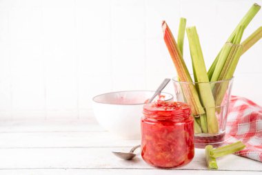 Pembe ve yeşil rengarenk tatlı reçel. Ev yapımı tatlı ravent konserveleri, beyaz ahşap masada küçük bir kavanozda, arka planda taze ravent ile.