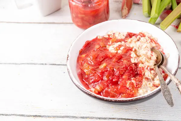 Kahvaltı kâsesinde tatlı ravent yulafı yaz tatili sağlıklı vegan yemekleri. Beslenme kahvaltısı ya da atıştırmalık. Beyaz ahşap masa fotokopi masasında, raventli reçelli, yoğurtlu organik ravent ve bir gecelik yulaf ezmesi.