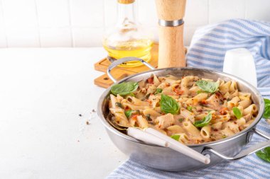 Son moda viral benimle tavuk makarnası evlen. Bir tencere yumuşak makarna ve kremalı ve peynirli sulu tavuk parçaları, sarımsaklı güneşte kurutulmuş domates sosu, nükteli fesleğen yaprağı, tabak ve demlikte.