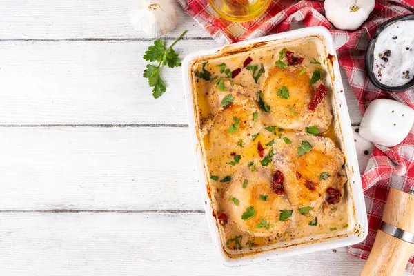 Evlen benimle tavuk, fırında tavuk budu, kremalı domates sosu, güneşte kurutulmuş domates, parmesan peyniri ve sert krema ile modaya uygun tavuk eti tarifi, ahşap ahşap masa ve yemek malzemeleri.