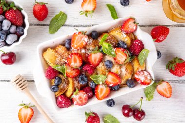 Yaz meyvesi ve Fransız tostu fırınlanmış güveç. Ev yapımı lezzetli Fransız tostu, kremalı kahvaltı pastası, kızarmış ekmek ve taze çilek, yabanmersini, ahududu ve kirazlı.