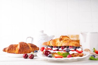 Krem şantili, taze meyve ve meyveli tatlı kahvaltı kruvasan sandviçi. Lezzetli bir yaz yemeği ya da içinde çilek, yabanmersini, kiraz, ahududu ve fındık bulunan taze kruvasanla atıştırmalık bir şeyler.