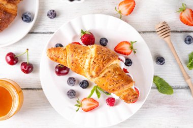 Krem şantili, taze meyve ve meyveli tatlı kahvaltı kruvasan sandviçi. Lezzetli bir yaz yemeği ya da içinde çilek, yabanmersini, kiraz, ahududu ve fındık bulunan taze kruvasanla atıştırmalık bir şeyler.