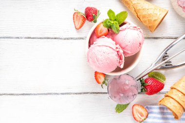 Yaz ferahlatıcı soğuk tatlı, lezzetli ve aromatik çilekli dondurma, seramik kasede ev yapımı meyve şerbeti, taze çilekler, beyaz ahşap arka planda dondurma külahları.