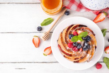 Taze meyve ve böğürtlenli yaz pastası. Geleneksel yuvarlak sünger keki, çilekli mevsimlik tatlı, ahududu, yabanmersini, bal ve şeker serpintileri, beyaz ahşap masa fotokopisi alanı