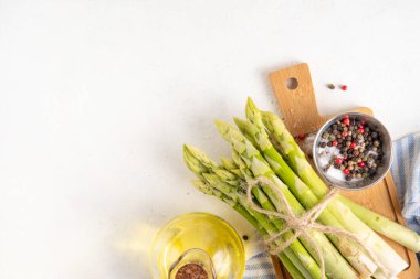 Çiğ organik kuşkonmaz mutfak masasının arka planında bir sürü ev yapımı yeşil kuşkonmaz pişirmeye ve kesme tahtasının üzerinde hazır. Yaz hasadı, yaz yemeği malzemeleri.