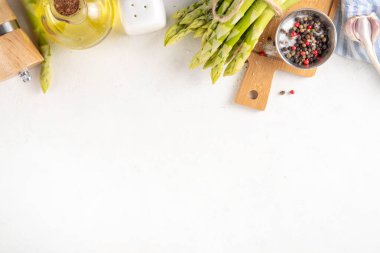 Çiğ organik kuşkonmaz mutfak masasının arka planında bir sürü ev yapımı yeşil kuşkonmaz pişirmeye ve kesme tahtasının üzerinde hazır. Yaz hasadı, yaz yemeği malzemeleri.