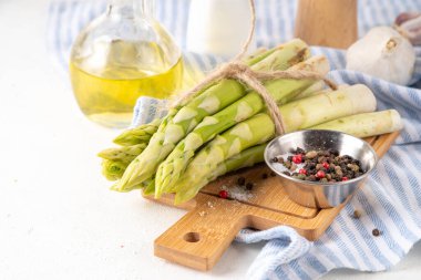 Çiğ organik kuşkonmaz mutfak masasının arka planında bir sürü ev yapımı yeşil kuşkonmaz pişirmeye ve kesme tahtasının üzerinde hazır. Yaz hasadı, yaz yemeği malzemeleri.