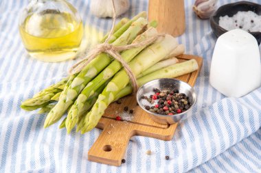 Çiğ organik kuşkonmaz mutfak masasının arka planında bir sürü ev yapımı yeşil kuşkonmaz pişirmeye ve kesme tahtasının üzerinde hazır. Yaz hasadı, yaz yemeği malzemeleri.