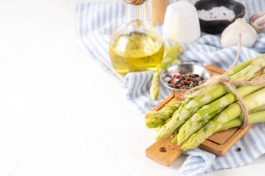 Çiğ organik kuşkonmaz mutfak masasının arka planında bir sürü ev yapımı yeşil kuşkonmaz pişirmeye ve kesme tahtasının üzerinde hazır. Yaz hasadı, yaz yemeği malzemeleri.