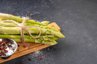 Çiğ organik kuşkonmaz mutfak masasının arka planında bir sürü ev yapımı yeşil kuşkonmaz pişirmeye ve kesme tahtasının üzerinde hazır. Yaz hasadı, yaz yemeği malzemeleri.