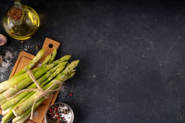 Çiğ organik kuşkonmaz mutfak masasının arka planında bir sürü ev yapımı yeşil kuşkonmaz pişirmeye ve kesme tahtasının üzerinde hazır. Yaz hasadı, yaz yemeği malzemeleri.