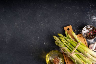 Çiğ organik kuşkonmaz mutfak masasının arka planında bir sürü ev yapımı yeşil kuşkonmaz pişirmeye ve kesme tahtasının üzerinde hazır. Yaz hasadı, yaz yemeği malzemeleri.