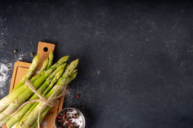 Çiğ organik kuşkonmaz mutfak masasının arka planında bir sürü ev yapımı yeşil kuşkonmaz pişirmeye ve kesme tahtasının üzerinde hazır. Yaz hasadı, yaz yemeği malzemeleri.