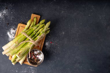 Çiğ organik kuşkonmaz mutfak masasının arka planında bir sürü ev yapımı yeşil kuşkonmaz pişirmeye ve kesme tahtasının üzerinde hazır. Yaz hasadı, yaz yemeği malzemeleri.