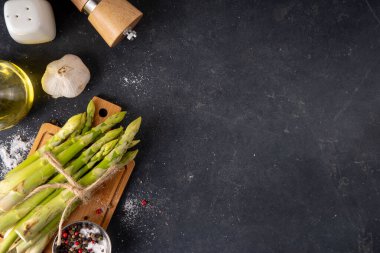 Çiğ organik kuşkonmaz mutfak masasının arka planında bir sürü ev yapımı yeşil kuşkonmaz pişirmeye ve kesme tahtasının üzerinde hazır. Yaz hasadı, yaz yemeği malzemeleri.