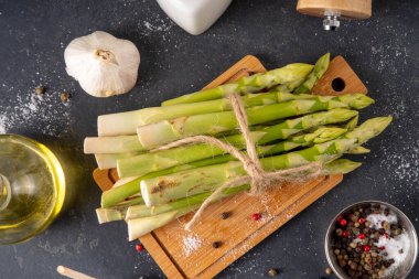 Çiğ organik kuşkonmaz mutfak masasının arka planında bir sürü ev yapımı yeşil kuşkonmaz pişirmeye ve kesme tahtasının üzerinde hazır. Yaz hasadı, yaz yemeği malzemeleri.