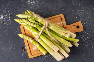 Çiğ organik kuşkonmaz mutfak masasının arka planında bir sürü ev yapımı yeşil kuşkonmaz pişirmeye ve kesme tahtasının üzerinde hazır. Yaz hasadı, yaz yemeği malzemeleri.