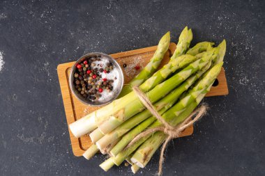 Çiğ organik kuşkonmaz mutfak masasının arka planında bir sürü ev yapımı yeşil kuşkonmaz pişirmeye ve kesme tahtasının üzerinde hazır. Yaz hasadı, yaz yemeği malzemeleri.