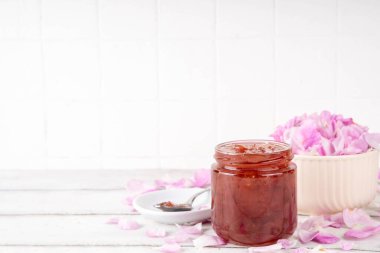 Gül yaprakları reçeli, tatlı çiçek tatlısı, ev yapımı konserve konserveler, organik tatlı gül yaprakları, şeker ve bal, beyaz masada küçük bir kavanozda. Alternatif ilaç, boğaz ağrısı ve soğuk algınlığı için ilaçlar.