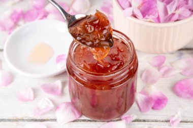 Gül yaprakları reçeli, tatlı çiçek tatlısı, ev yapımı konserve konserveler, organik tatlı gül yaprakları, şeker ve bal, beyaz masada küçük bir kavanozda. Alternatif ilaç, boğaz ağrısı ve soğuk algınlığı için ilaçlar.