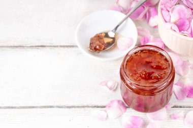 Gül yaprakları reçeli, tatlı çiçek tatlısı, ev yapımı konserve konserveler, organik tatlı gül yaprakları, şeker ve bal, beyaz masada küçük bir kavanozda. Alternatif ilaç, boğaz ağrısı ve soğuk algınlığı için ilaçlar.