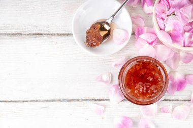 Gül yaprakları reçeli, tatlı çiçek tatlısı, ev yapımı konserve konserveler, organik tatlı gül yaprakları, şeker ve bal, beyaz masada küçük bir kavanozda. Alternatif ilaç, boğaz ağrısı ve soğuk algınlığı için ilaçlar.