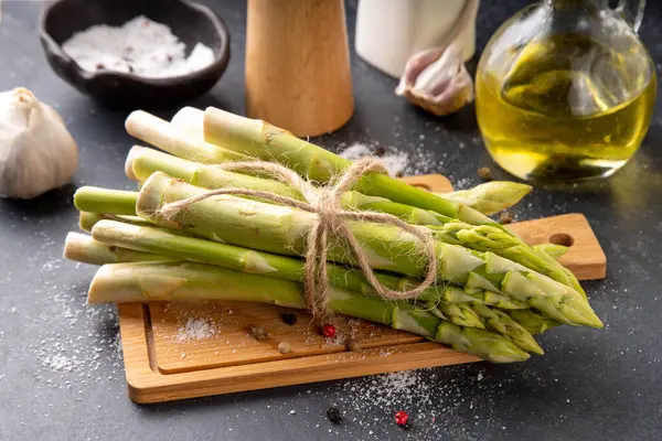 Çiğ organik kuşkonmaz mutfak masasının arka planında bir sürü ev yapımı yeşil kuşkonmaz pişirmeye ve kesme tahtasının üzerinde hazır. Yaz hasadı, yaz yemeği malzemeleri.